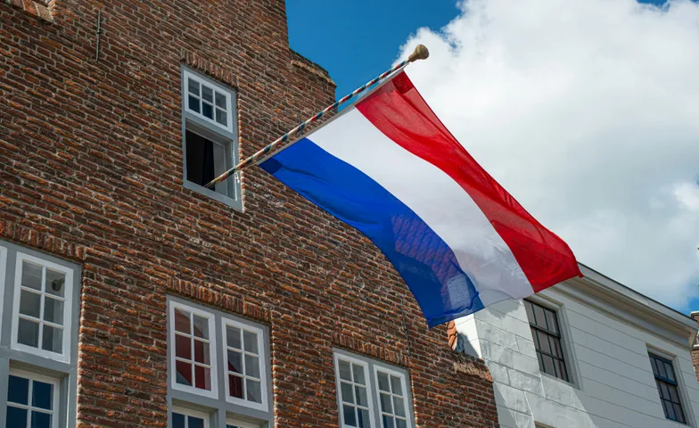 Nederlandse vlag aan een gevel, uitgestoken tegen een blauwe lucht