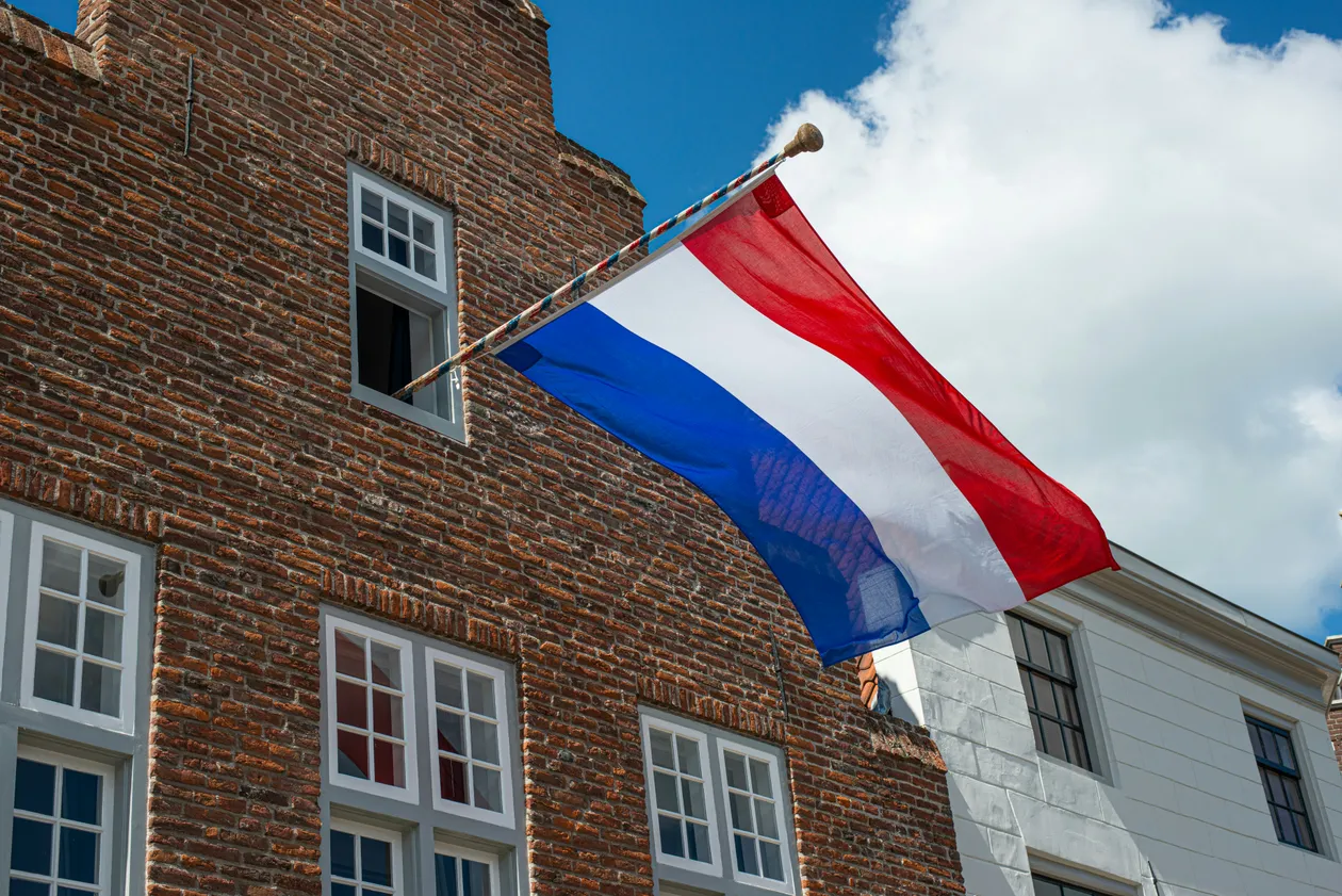 Nederlandse vlag aan een gevel, uitgestoken tegen een blauwe lucht